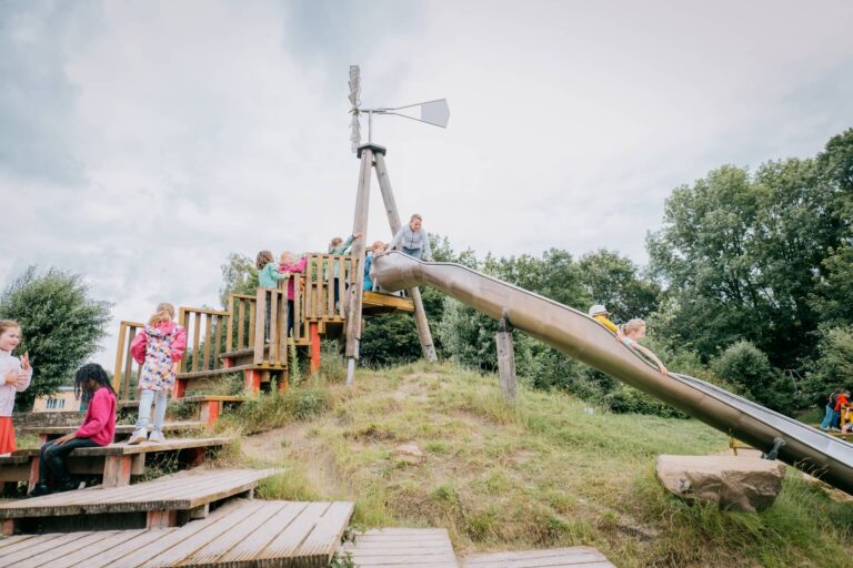 Glückliche Kinder, die rutschen und zur Rutsche anstehen von etwas weiter weg.