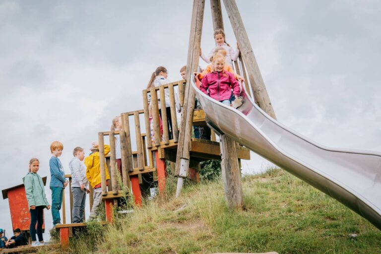 Glückliche Kinder, die rutschen und zur Rutsche anstehen.