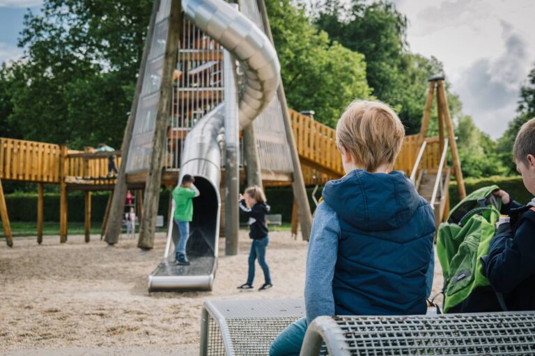 Ein kleiner Junge schaut auf spielende Kinder an dem großen Spielturm.