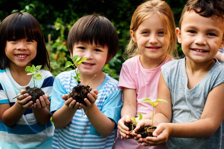 Glückliche Kindergarten-Kinder, die Setzlinge in der Hand halten.